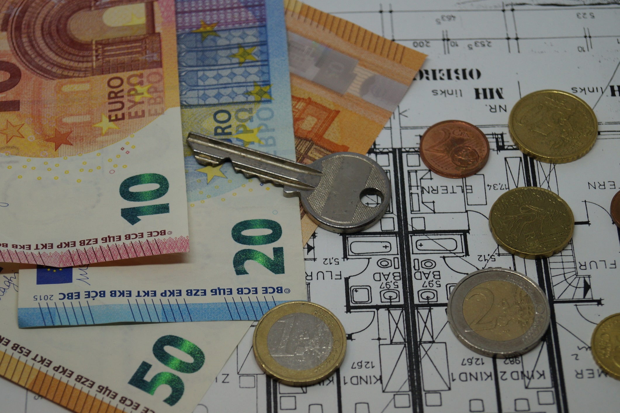 Wohnungschlüssel und Geldscheine liegen auf Wohnungspapieren und Grundriss